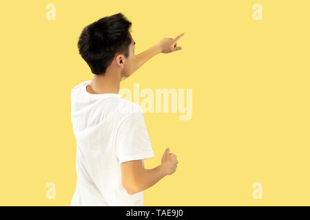 Jeune homme coréen demi-longueur du portrait sur fond jaune studio. Modèle masculin en chemise blanche. Pointant vers le haut à l'endroit pour votre annonce. Concept des droits de l Banque D'Images