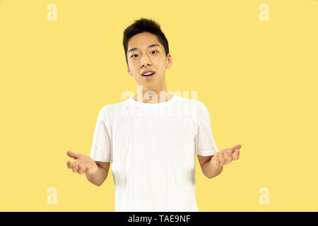 Jeune homme coréen demi-longueur du portrait sur fond jaune studio. Modèle masculin en chemise blanche. Souriant et accueillant. Concept d'émotions humaines, faces avant Banque D'Images