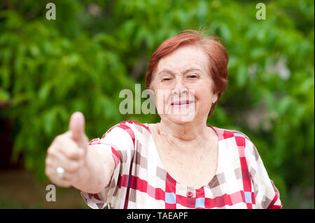 Femme âgée avec thumb up laughing outdoors. Les cadres supérieurs. En regardant la caméra. 70. Banque D'Images