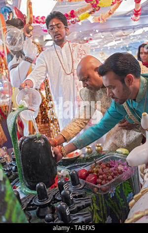 Une adolescente pandit et deux de fervents adorateurs de verser de l'eau au-dessus et touchez un Shiva Lingam dans un temple hindou de la Jamaïque, Queens, New York. Banque D'Images