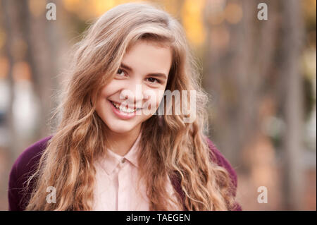 Smiling blonde adolescente 14-16 ans avec de longs cheveux bouclés à l'extérieur. En regardant la caméra. Magnifique portrait. Le bonheur. Banque D'Images