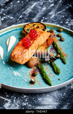 Tranche de saumon grillé garni d'asperges vertes cuites, tomates cerise et citron au cari Banque D'Images