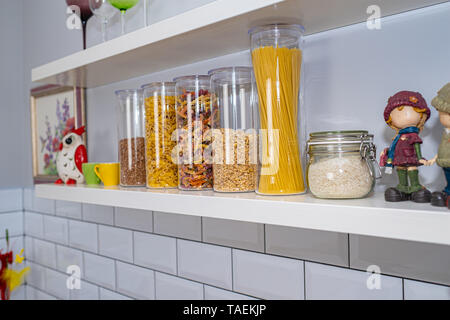 Divers produits alimentaires non cuites dans des bocaux en verre disposées sur des étagères blanches ar la cuisine Banque D'Images