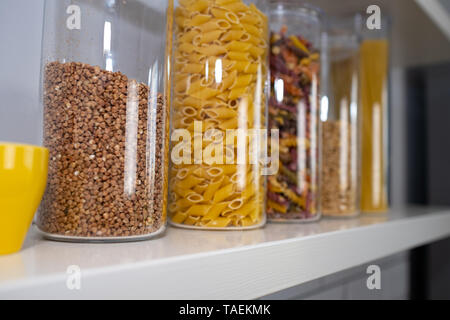 Divers produits alimentaires non cuites dans des bocaux en verre disposées sur des étagères blanches ar la cuisine Banque D'Images