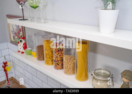 Divers produits alimentaires non cuites dans des bocaux en verre disposées sur des étagères blanches ar la cuisine Banque D'Images