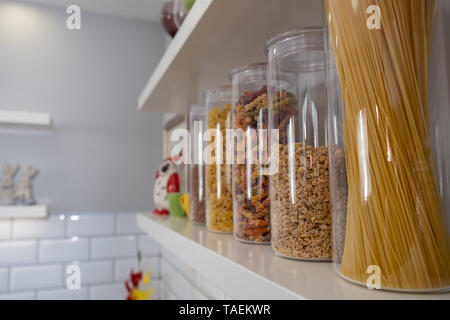 Divers produits alimentaires non cuites dans des bocaux en verre disposées sur des étagères blanches ar la cuisine Banque D'Images