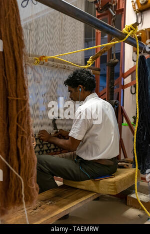 Vue verticale d'un homme à l'écoute de son iphone tout en utilisant un ancien métier à tisser vertical en Inde. Banque D'Images