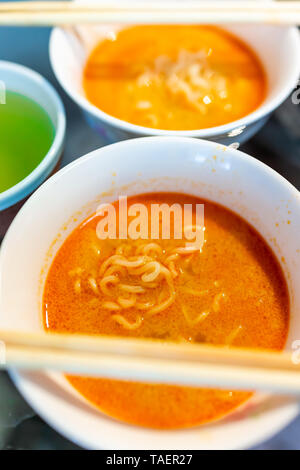 Gros plan macro rouge épicé de nouilles ramen soup bowl avec des baguettes asiatiques japonais thé vert et repas Banque D'Images