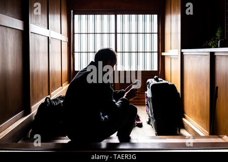 Maison machiya japonais traditionnel ou ryokan avec porte coulissante entrée papier et la lumière avec homme assis tenant l'architecture téléphonique Banque D'Images