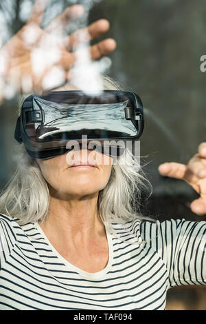 Portrait of mature femme derrière la vitre à l'aide de lunettes de réalité virtuelle Banque D'Images