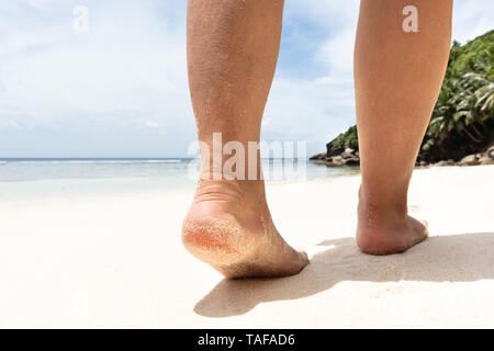 La section basse de Woman's pieds marchant sur une plage de sable vers la mer Banque D'Images
