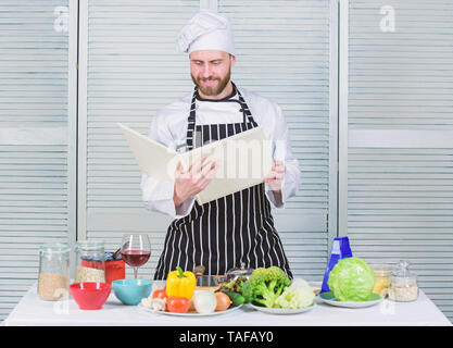 Guy lire livre de recettes. Concept d'arts culinaires. Apprendre l'homme recette. Améliorer les compétences de cuisson. Livre des recettes de famille. Guide de cuisson ultime pour les débutants. Selon recette. Chef barbu homme à la cuisson des aliments. Banque D'Images