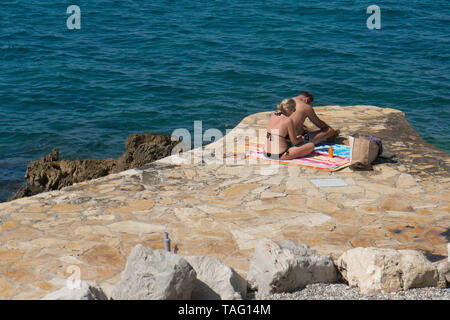 Porec , Croatie 5 Septembre 2018 : les touristes bronzer sur la côte rocheuse. Une femme Un homme se frotte avec protection solaire. Banque D'Images