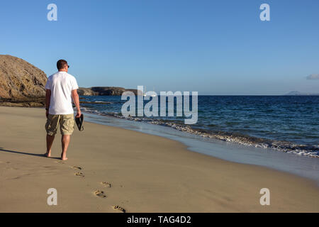 Un adulte homme marche le long d'un désert tranquille plage de Papagayo à Lanzarote, pris dans le soleil du soir la vue montre l'arrière de l'homme d'âge moyen Banque D'Images