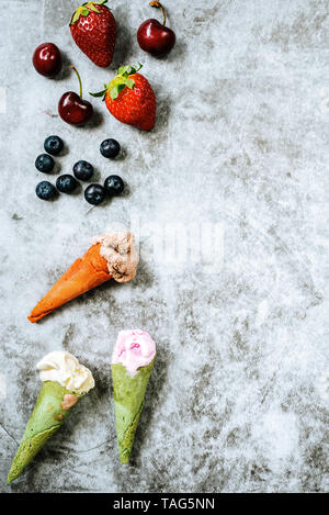 Les fruits rouges comme les fraises et les bleuets, cerises en regard de trois glaces en cône, sur fond noir en clair avec copie espace pour le texte. Banque D'Images