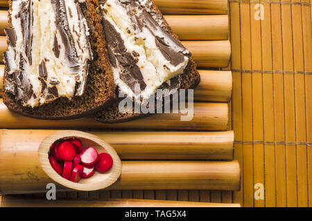 Sandwich avec pain de blé noir grossier et sweet curd et chocolat noir sur un stand de bambou et de bambou serviette avec perles de corail rouge. Il simple délicieux Banque D'Images