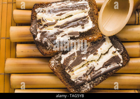 Sandwich avec pain de blé noir grossier et sweet curd et chocolat noir sur un stand de bambou et de bambou serviette. Délicieux petit déjeuner santé simple en e Banque D'Images