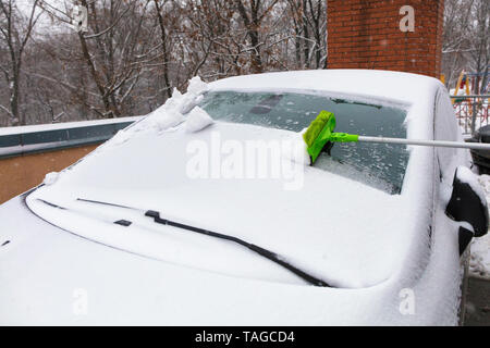 Le pliage long green brush nettoie la neige d'un pare-brise de la voiture Banque D'Images