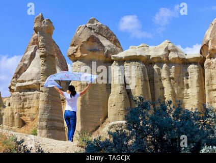 Une jeune femme tient un voile bleu bigarrée sur sa tête, debout dans le vent entre d'énormes roches et dans la vallée du miel de la Cappadoce. Banque D'Images