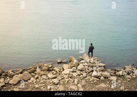 Pêcheur asiatique solitaire debout sur les rochers en face de belle eau Banque D'Images
