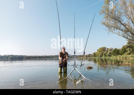 Aventures de pêche, pêche à la carpe. Bottes en caoutchouc vert avec pêcheur Banque D'Images
