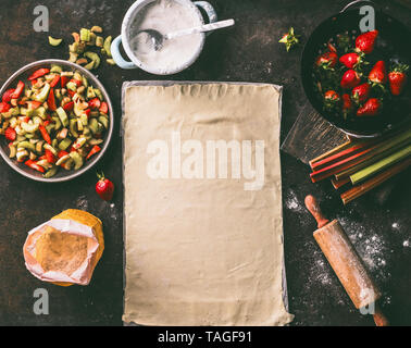 Feuille de pâte feuilletée sur une table de cuisine rustique avec la rhubarbe et fraises Ingrédients pour gâteau tarte, vue d'en haut. Cuisson saisonnière. L'alimentation biologique. L'étape Banque D'Images