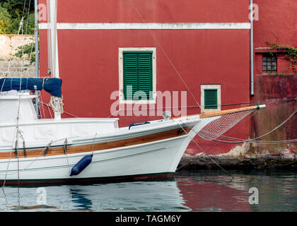 Vieux Bateau à voile en bois blanc dans l'eau en face de la maison rouge aux volets verts Banque D'Images