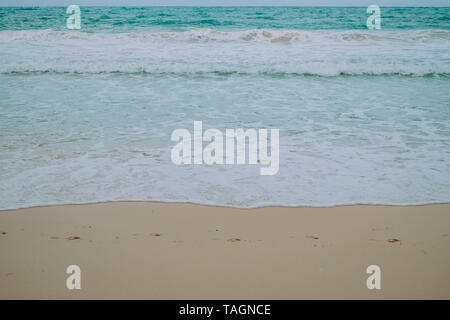 Empreintes de pas sur le sable fin, les vagues de la mer et de la mousse dans la plage. Focus sélectif. Copier l'espace. Minimaliste. Banque D'Images