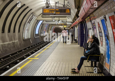 Une dame est assise sur un banc sur une plate-forme tranquille à Bond Street Londres gare souterraine alors qu'elle attend un train ligne centrale d'arriver. Banque D'Images