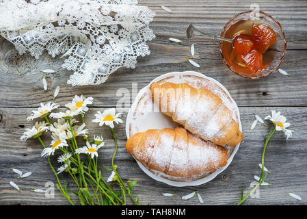 Belle composition : deux croissants, bouquet de fleurs Daisy peach, confiture et white lacy nappes sont sur un vieux fond de bois Banque D'Images