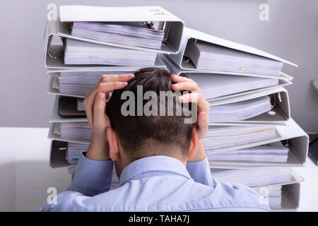 Vue arrière du souligné Businesswoman Pointing en face de dossiers empilés Banque D'Images