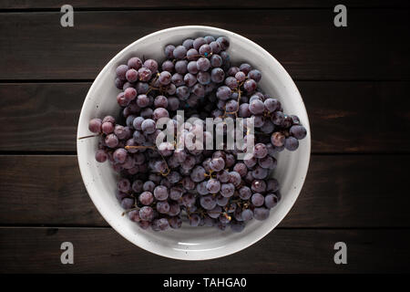 Vue de dessus de raisins rouges frais dans le bol blanc sur la table en bois. Style alimentaire sombre Banque D'Images