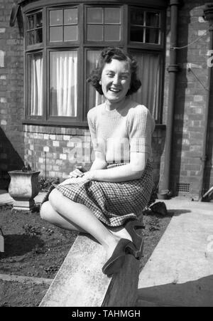 La vie de famille en UK c1950 Une jeune femme pose sur un mur à l'avant d'une maison dans un magnifique portrait. Photo par Tony Henshaw Banque D'Images