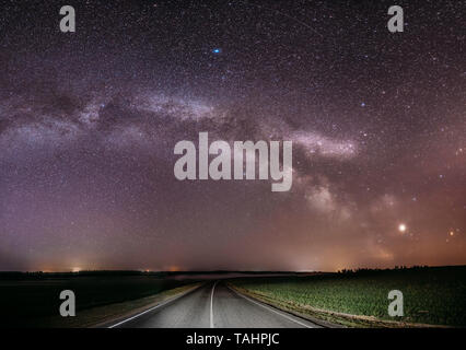 Nuit Magenta Ciel étoilé au-dessus de pays route asphaltée en campagne et champ vert. Vue de la Nuit des étoiles brillant naturel et Voie lactée. Panorama Banque D'Images