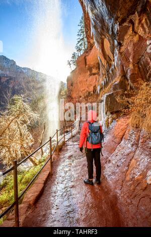 Randonneur en face de cascade, chutes d'eau de roche en surplomb, sentier de randonnée glacée Emerald Pools Trail en hiver, Zion National Park, Utah, USA Banque D'Images