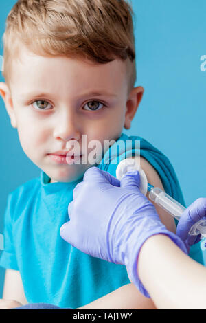 Concept de vaccination. Femme médecin vaccinant cute little boy sur fond bleu, libre. Banque D'Images