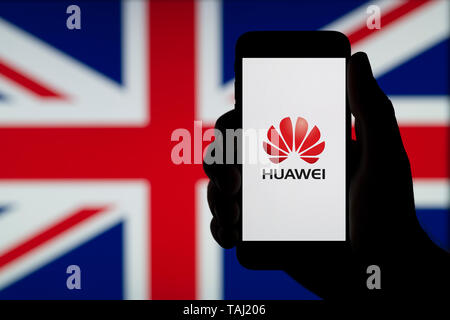 La silhouette d'une main d'un homme est titulaire d'un smartphone affichant le logo de l'entreprise chinoise Huawei, avec un drapeau britannique dans l'arrière-plan (usage éditorial uniquement). Banque D'Images