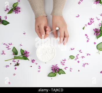 Deux femmes et un pot avec de la crème épaisse et des fleurs roses avec des feuilles vertes, vue du dessus, concept de procédures anti-âge pour le rajeunissement et moistu Banque D'Images