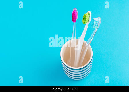 Trois brosses à dents colorées en plastique en verre sur fond bleu, Close up Banque D'Images