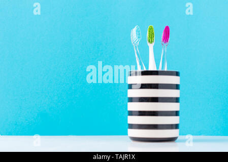 Trois brosses à dents colorées en plastique en verre sur fond bleu, Close up Banque D'Images