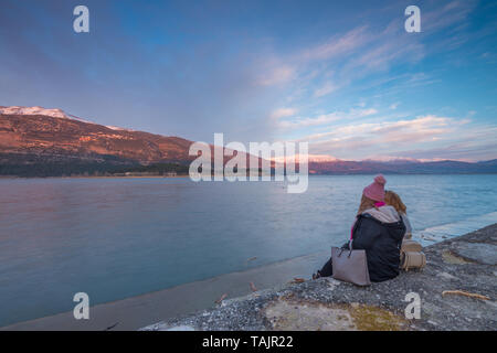 Deux amies regarder le coucher du soleil au bord du lac, regardant les montagnes et le ciel peint. Femme amis regardant le coucher du soleil. Banque D'Images