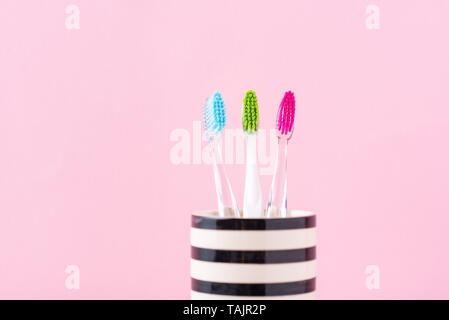 Trois brosses à dents colorés en plastique en verre sur fond rose, Close up Banque D'Images