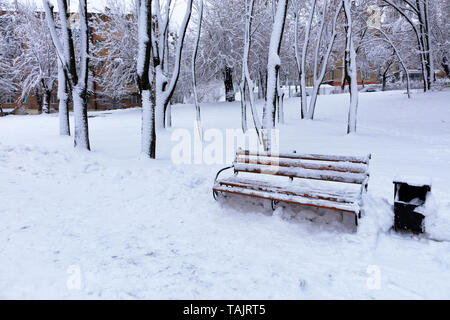 Belle vue sur le banc en bois dans l'allée du parc de la ville couverte de neige, sur le côté gauche de l'espace de publicité copie Banque D'Images