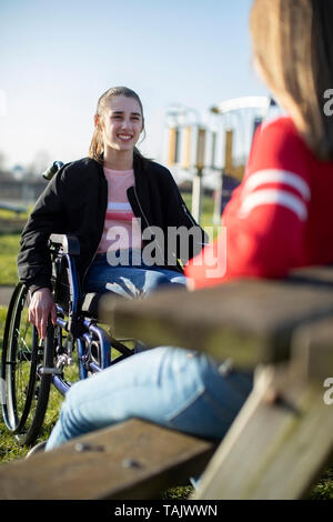 Teenage Girl In Wheelchair Talking With Friend In Park Banque D'Images