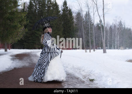 Femme âgée dans une robe gothique dans un chapeau avec un parapluie noir sur la nature en hiver Banque D'Images