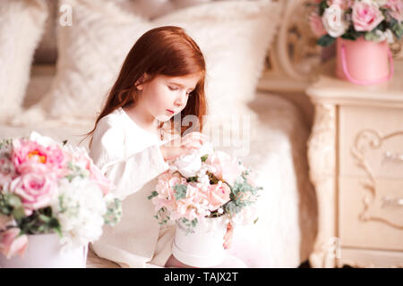 Mignon bébé fille 3-4 ans holding Flowers siégeant à la salle close up. La saison du printemps. L'enfance. Banque D'Images