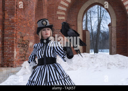 Une femme âgée dans une robe gothique avec un corbeau noir hat sur la nature en hiver Banque D'Images