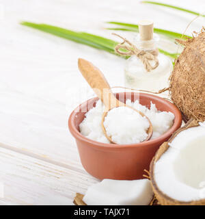 Arrière-plan de la noix de coco, noix de coco, l'huile dans un bol d'argile et de verre pot et cuillère sur la table en bois blanc Banque D'Images