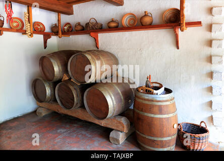 Des tonneaux de vin en bois Vintage céramique peint, bols, assiettes et de bidons sur une planche en bois sur le mur, un panier en osier avec verrerie dans l'intérieur d'un Banque D'Images