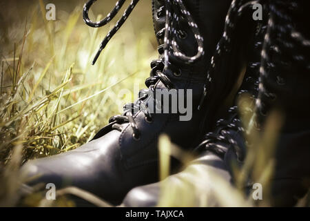 Les Noirs de l'armée en cuir bottes avec lacets noirs et blancs debout dans l'herbe, éclairé par la lumière du soleil. Banque D'Images